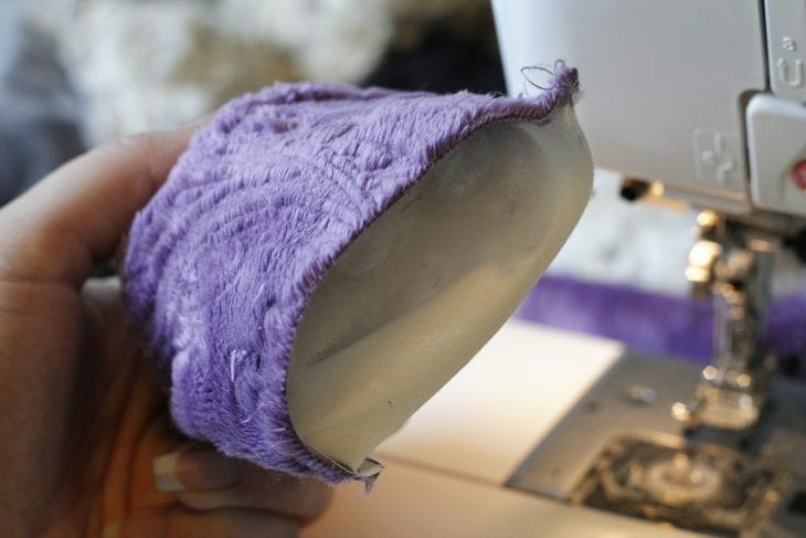 Hand holding purple fabric in front of sewing machine image.
