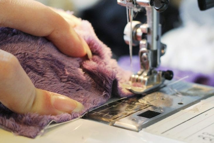 Fingers pushing plush fabric through a sewing machine image.