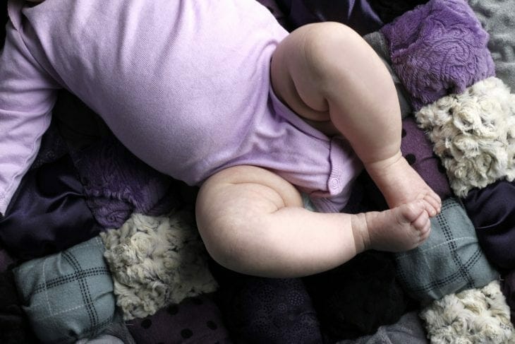 Little girl in purple onesie laying on a purple puff blanket image.