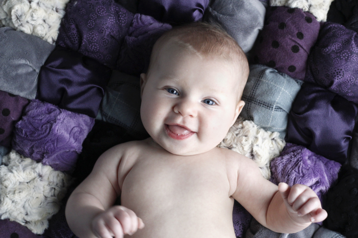 Smiling baby girl laying on purple puff quilt image.