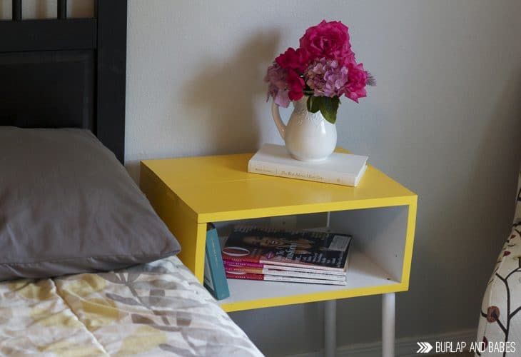 Yellow side table next to a bed with pink flowers in a vase on top image.