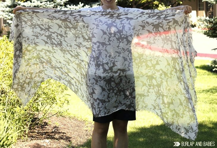Woman holding up a large, sheer scarf image.