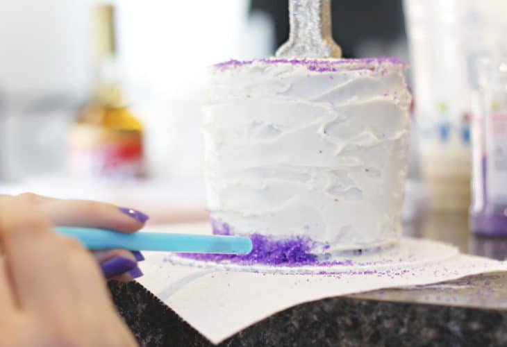 Blue straw blowing purple sugar on white cake image.