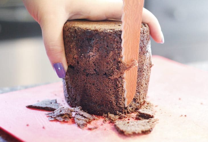 Hand using a knife to cut edges from cake image.