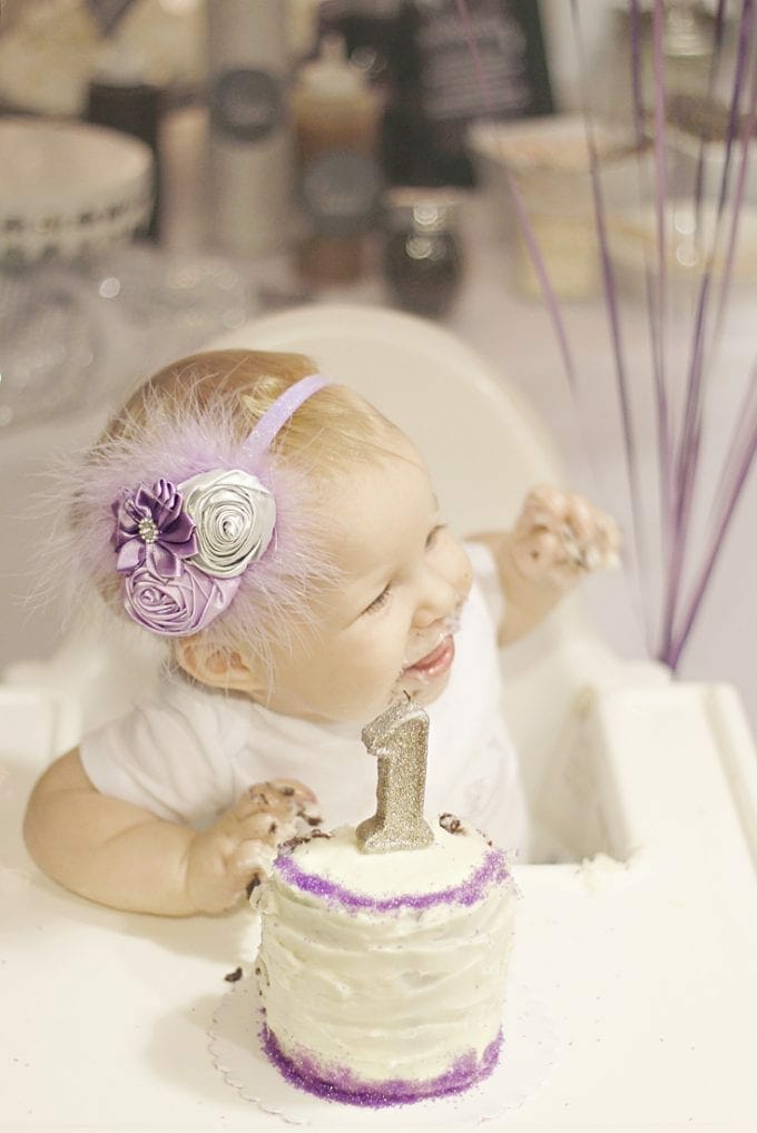 Pretty little girl in purple headband eating first birthday cake image.