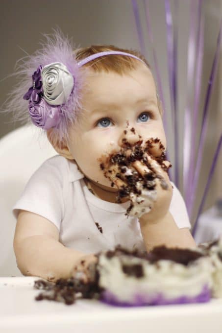 Little girl in purple headband with chocolate cake all over her face and hands image.