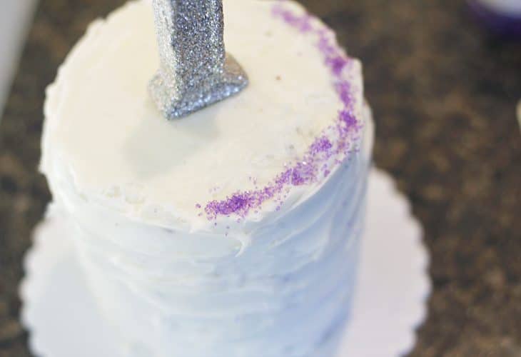 White cake with purple sugar in edges and 1 candle image.