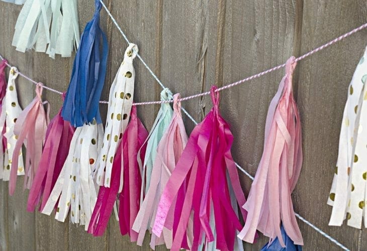 Pink, white, gold, blue tassels tied to a fence wall image.