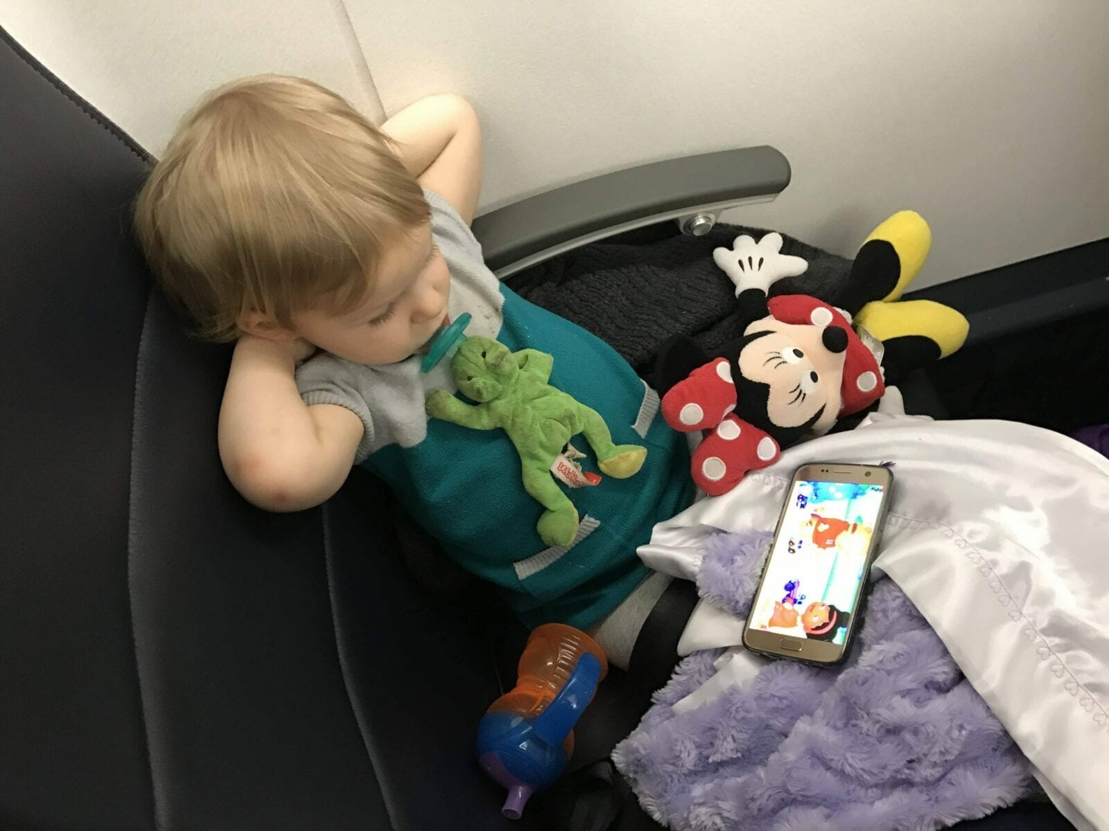 Child in airplane seat with Minnie Mouse image.