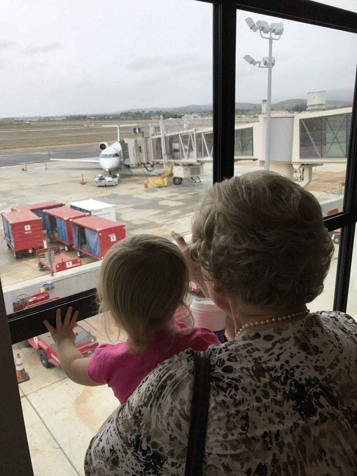 Grandma holding child up to window in airport image.