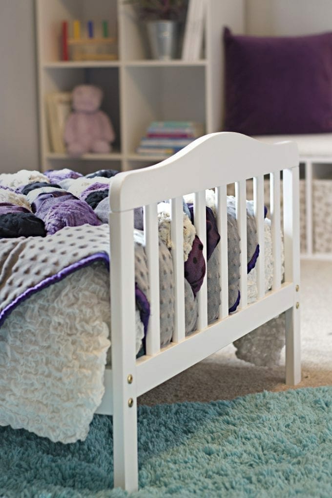 Toddler white bed frame with purple quilt image.