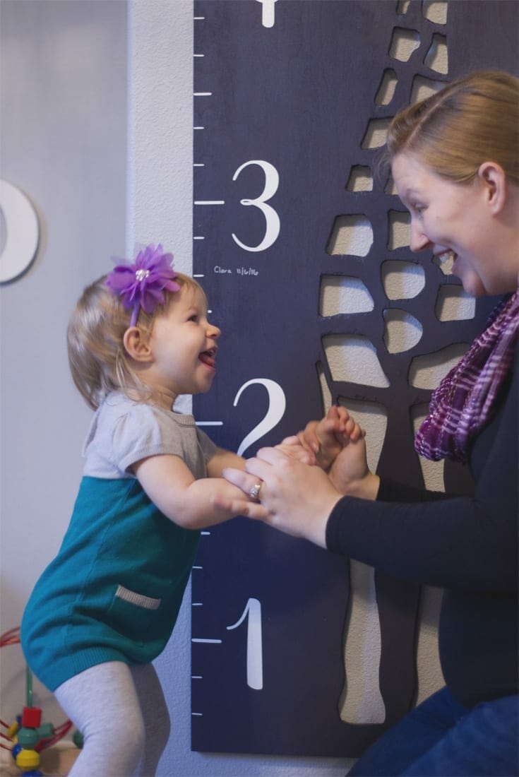 Little girl and Mom laughing in front of giraffe growth chart image.