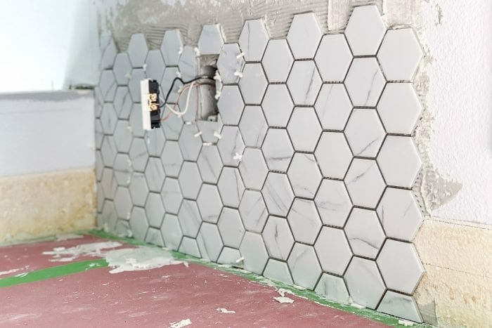 Installing tiles on the kitchen wall with FrogTape on the corners to protect the counter