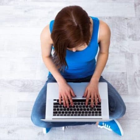 Top view portrait of a young woman sitting on the floor and typing on laptop
