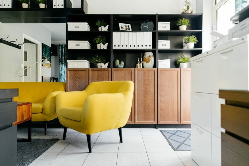 Creative yellow armchairs placed near wooden coffee table in cozy living room with creative shelves decorative houseplants