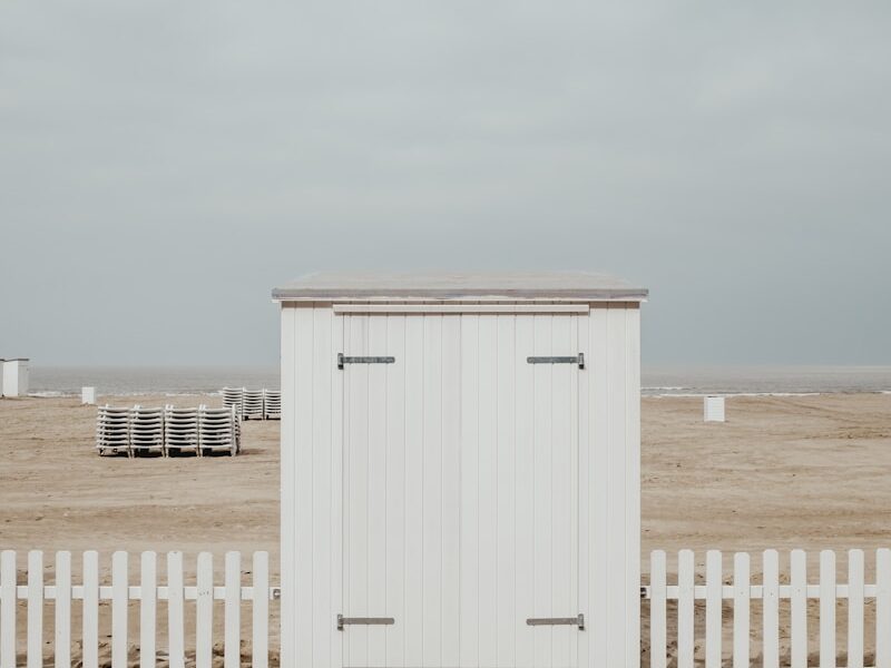 white wooden shed on sand under white clouds