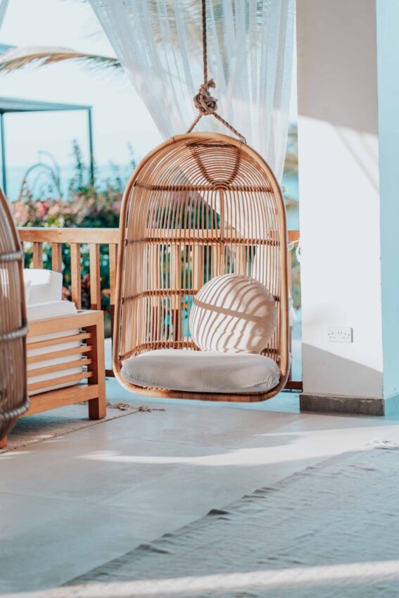 Rattan hanging chair with cushions on a bright, sunlit terrace. Perfect for relaxation.