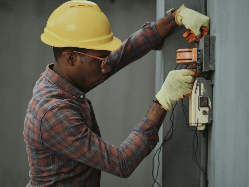 man in brown and white plaid dress shirt and yellow hard hat holding black and orange