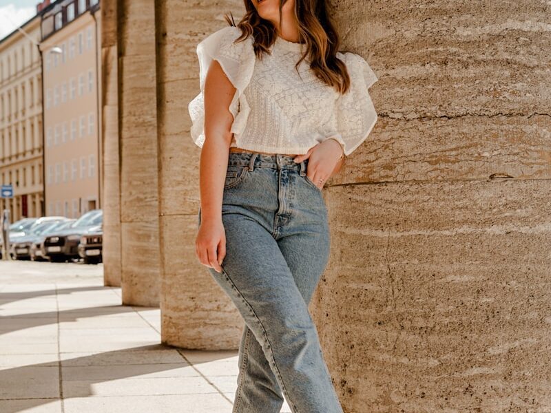 woman in white tank top and blue denim jeans standing on brown concrete floor during daytime