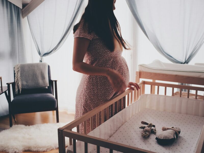 woman in white lace sleeveless dress standing beside brown wooden crib
