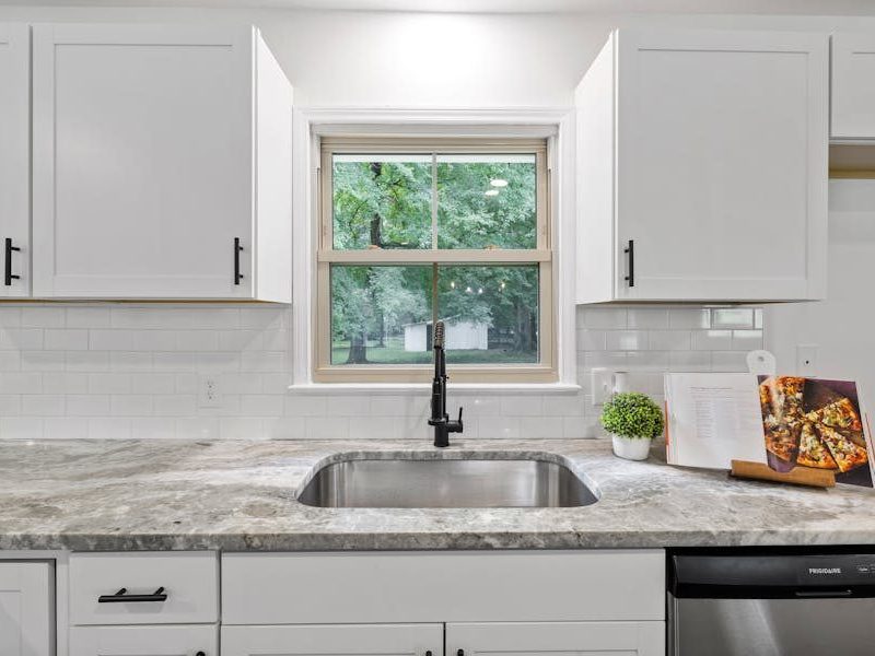 Bright kitchen interior featuring white cabinets, granite countertop, and a window with a view.