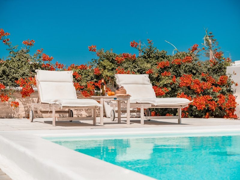a pool with chairs and a table by it with flowers on the side