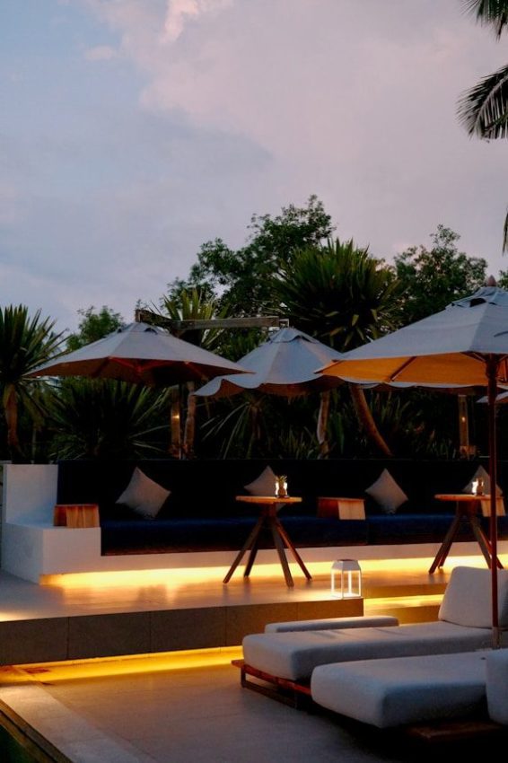Lounge chairs and umbrellas by a pool at dusk.