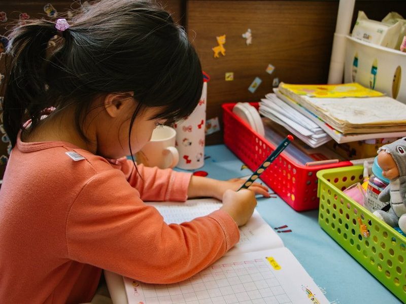 girl in pink long sleeve shirt writing on white paper