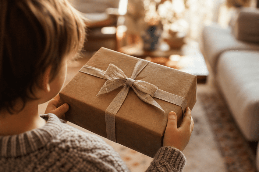 Child holding wrapped gift box with ribbon in cozy room.
