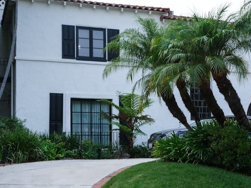 White stucco house with palm trees and lush greenery.