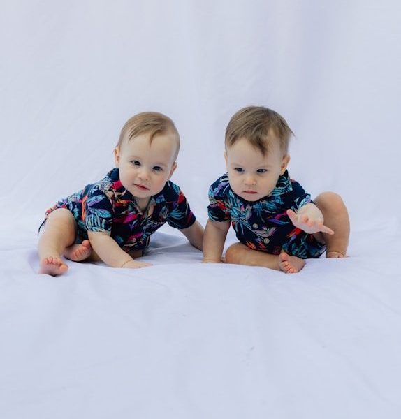 Two babies in matching floral shirts on white background