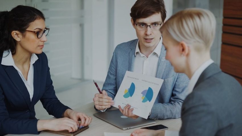Three professionals discussing charts in a meeting.