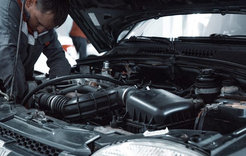A mechanic in a grey uniform inspecting the engine of a car