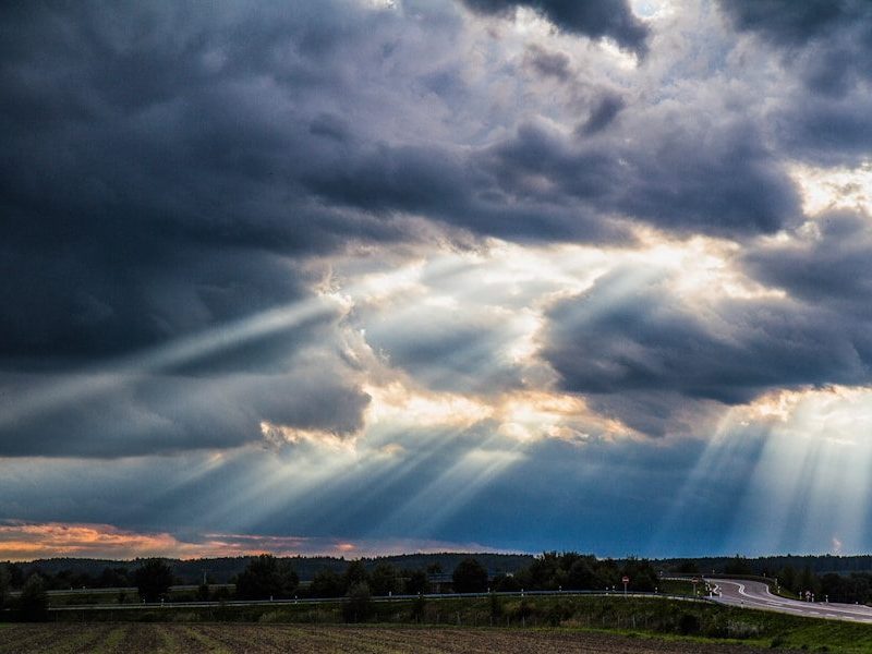 Sunlight streaming through dark storm clouds over a rural road and field