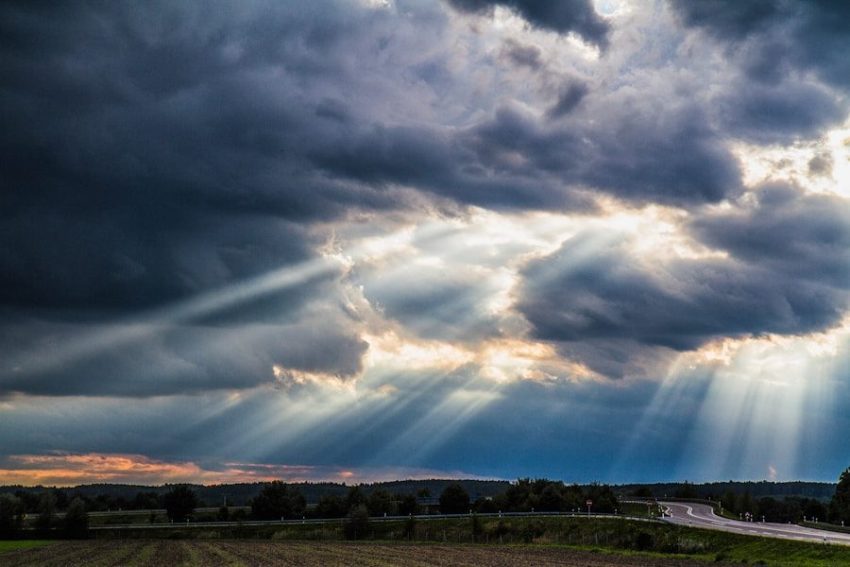 Sunlight streaming through dark storm clouds over a rural road and field