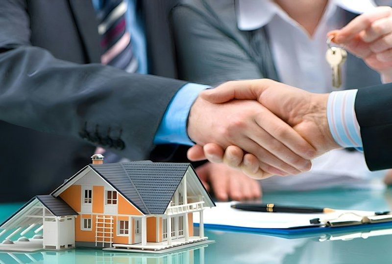 Two men shaking hands over a house model and keys