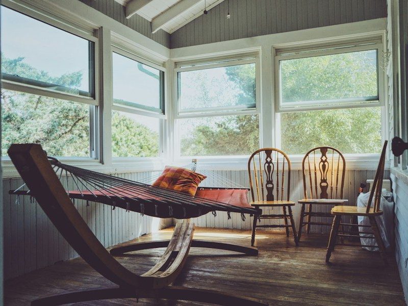 photography of grey, white, and brown wooden house interior with three brown wooden Windsor chairs beside brown hammock with glass windows