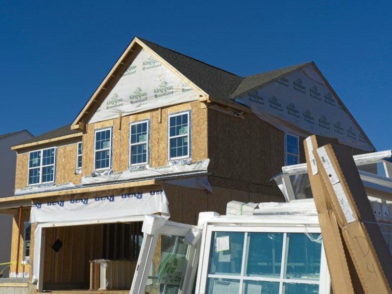 A house under construction with plywood walls and stacked windows in the foreground
